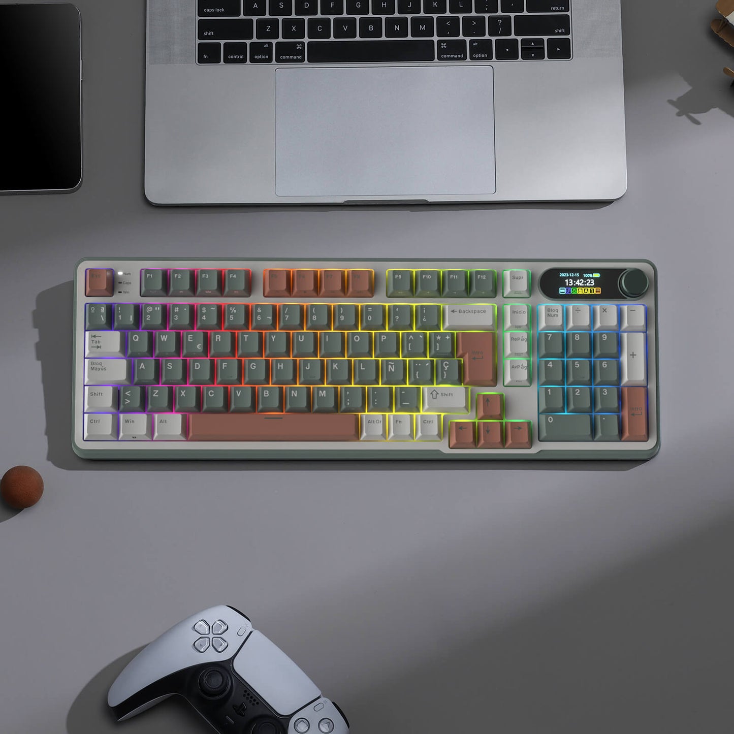 Colorful mechanical keyboard on a desk with a laptop and gaming controller.